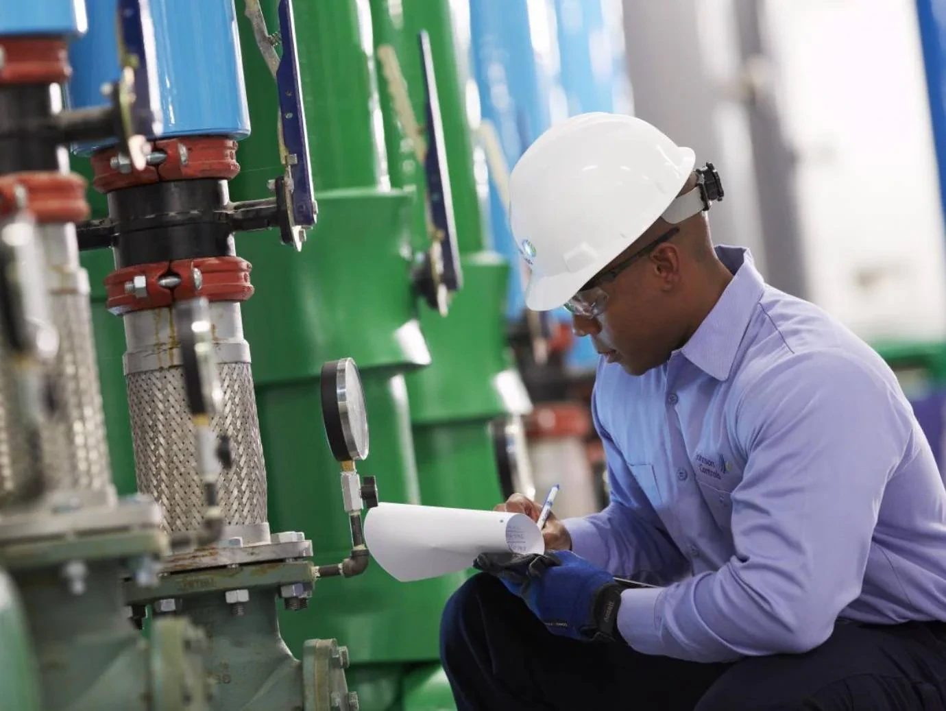 HVAC technician recording equipment readings beside mechanical system piping